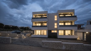 A modern multi-story building with balconies and large windows, surrounded by a stone wall and a gravel driveway. - Mare Room with Balcony and Shared Pool (Novalja)