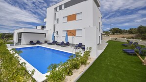 A modern two-story building with a swimming pool, outdoor seating, and a well-maintained lawn. - Mare Room with Balcony and Shared Pool (Novalja)