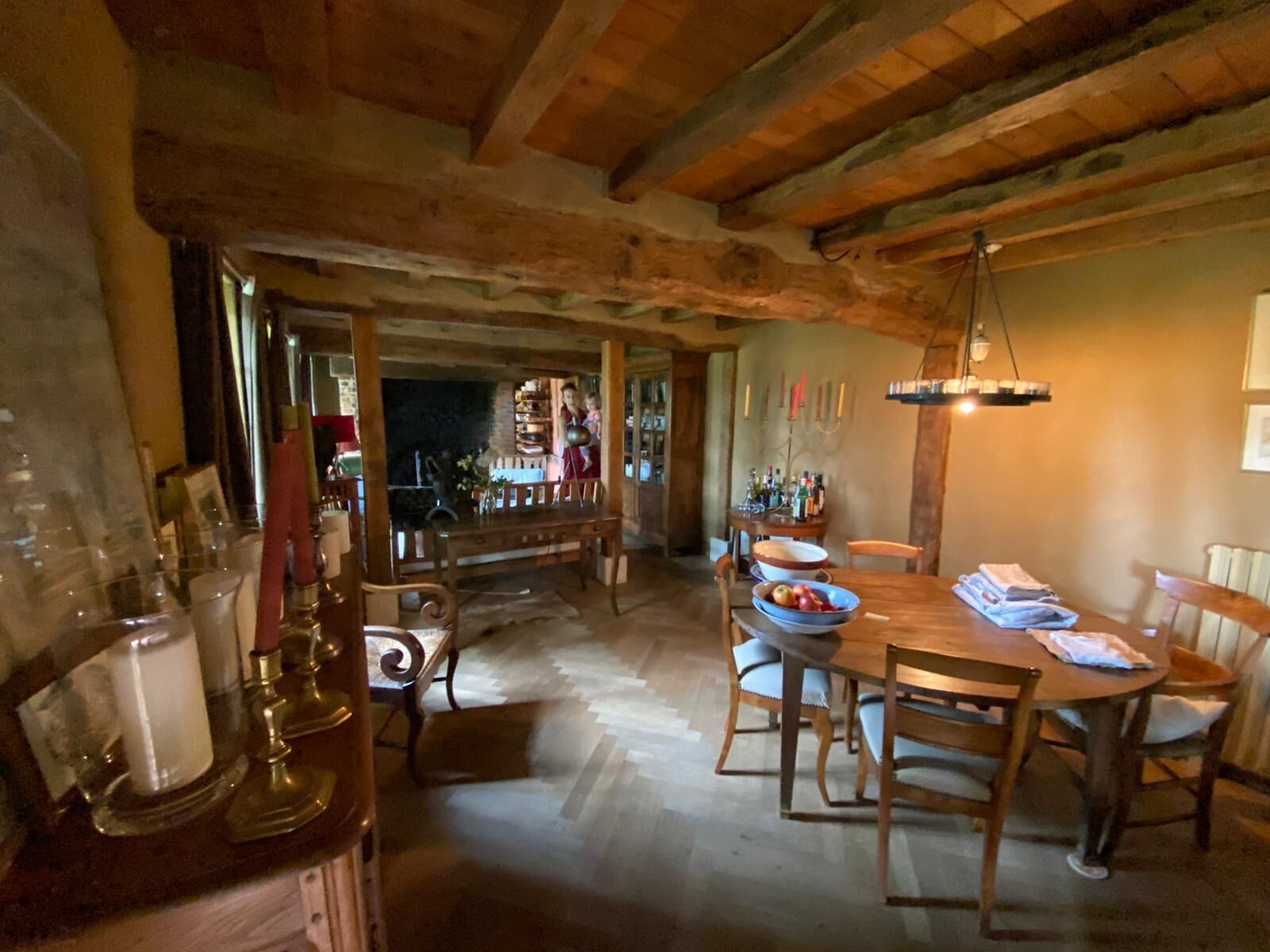 Uma zona de refeições rústica com mesa e cadeiras de madeira, área de bar com garrafas e copos, e um candelabro.