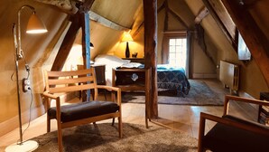 Un dormitorio acogedor en el ático, con techo inclinado, vigas de madera, una cama con colcha estampada, un escritorio con lámpara y una silla.
