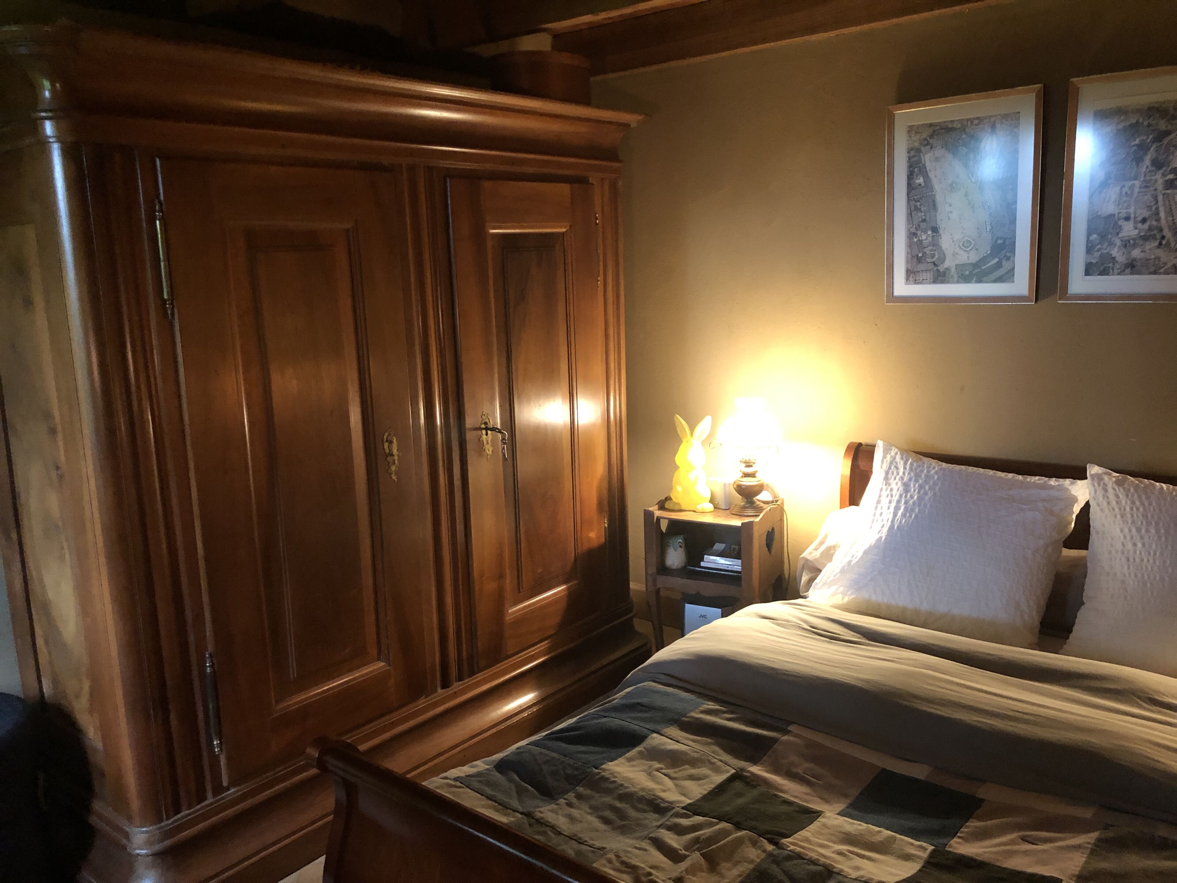 Een slaapkamer met een houten garderobe, een nachtkastje met een lamp, en een bed met een sprei.