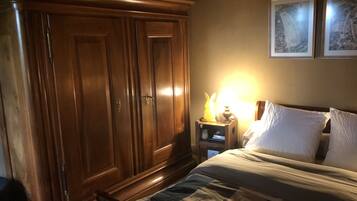 Een slaapkamer met een houten garderobe, een nachtkastje met een lamp, en een bed met een sprei.