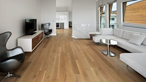 Een moderne woonkamer met een flatscreen televisie, zwart-wit meubels, een houten vloer en grote ramen met uitzicht op de stad.