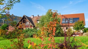 Een tweelaags huis met een balkon, omgeven door een verzorgde tuin met verschillende planten en bloemen.