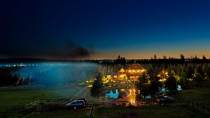 Una vista notturna di un lodge con un edificio grande illuminato da luci, circondato da alberi e un lago avvolto dalla nebbia.