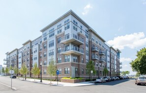 Un edificio de apartamentos de varios pisos con un diseño moderno, con balcones y un estacionamiento con varios automóviles.