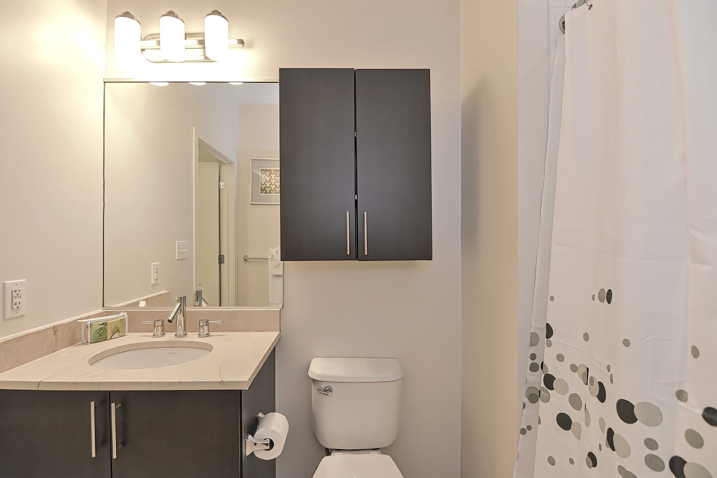 A bathroom with a sink, mirror, toilet, and dark cabinets.