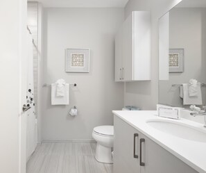 Un baño moderno con inodoro, lavabo y espejo. Toallas cuelgan de un perchero y hay un cuadro en la pared.