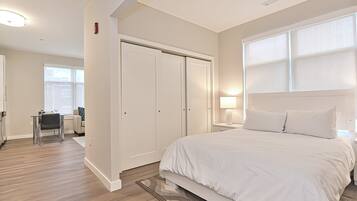 A bedroom with a large bed, a desk with a chair, a wardrobe, and a window with blinds.