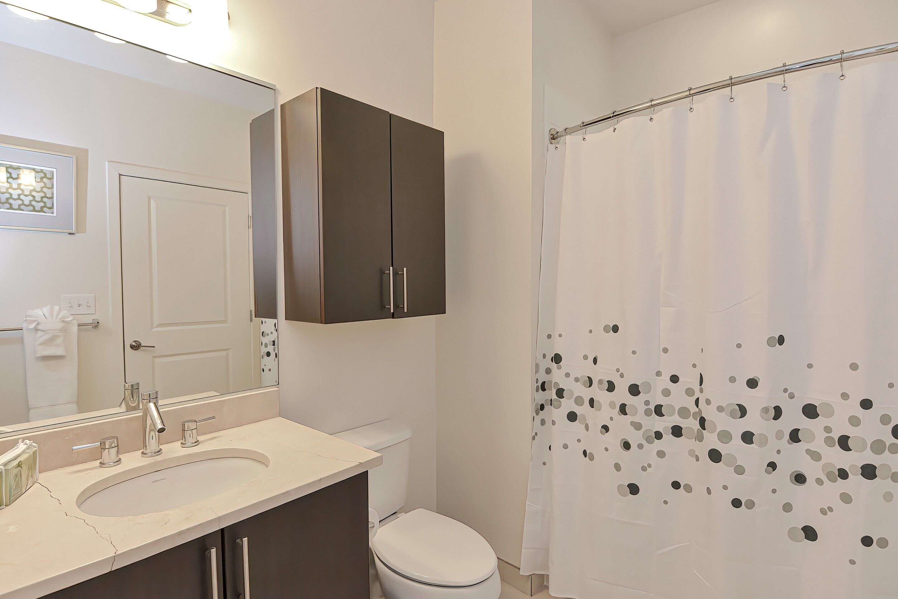 A bathroom with a sink, mirror, cabinet, toilet, and shower curtain.