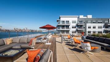 Terraza en la azotea con mobiliario exterior, una chimenea y vistas del horizonte urbano y el agua.