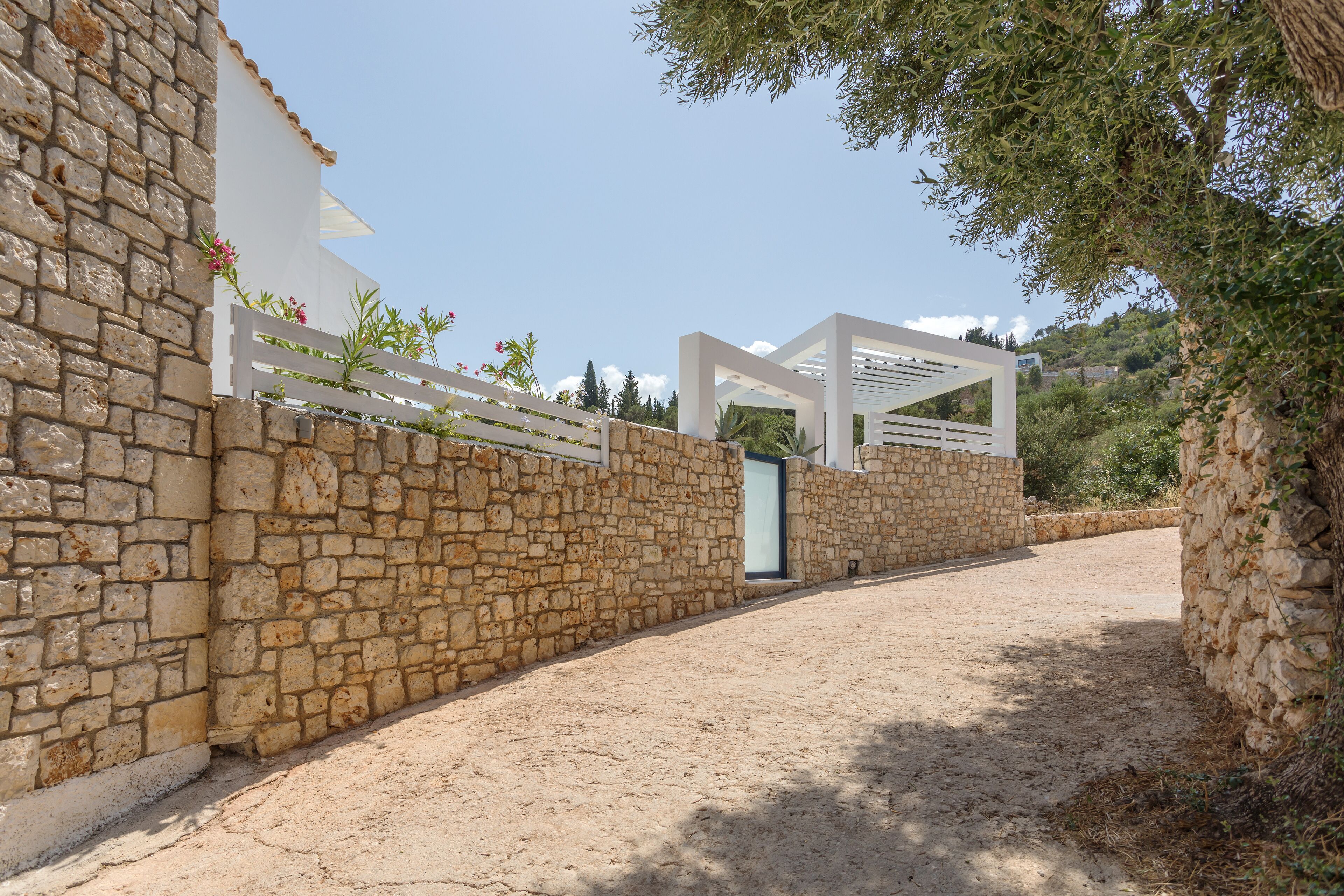Um muro de pedra com um portão branco e uma estrutura de pérgola.