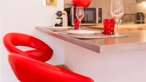 A modern kitchen with red accents, a dining area with red chairs, and a small island with a microwave and wine glasses. - 1 Bedroom Flat - Wifi, Air Conditionning / 1 to 5 People (Aix-en-Provence)