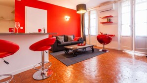 A modern living room with a red accent wall, a black sofa, a red chair, a coffee table, and a pendant light. - 1 Bedroom Flat - Wifi, Air Conditionning / 1 to 5 People (Aix-en-Provence)