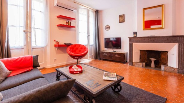 A living room with a sofa, a red chair, a coffee table, a TV, a fireplace, and red shelves. - 1 Bedroom Flat - Wifi, Air Conditionning / 1 to 5 People (Aix-en-Provence)