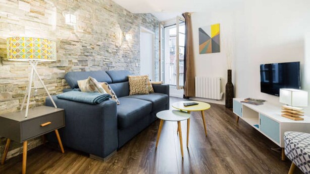 A modern living room with a stone wall, a sofa, a coffee table, a TV, and a lamp. - 1 Bedroom Flat Quartier Rotonde - Lift, Wifi, Air Conditionning / 1 to 6 People (Aix-en-Provence)