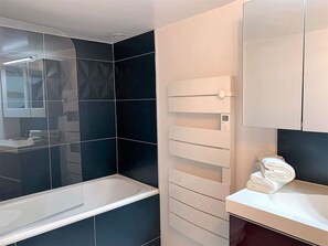 Une salle de bain moderne avec un grand miroir, un lavabo blanc et un mur recouvert de carreaux noirs.