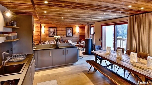 A modern kitchen with wooden ceiling, a dining area with a long table, and a view of the outdoors.