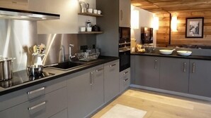 A modern kitchen with grey cabinets, stainless steel appliances, and wooden ceiling beams.