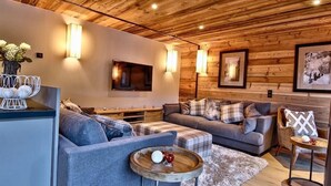 A cozy living room with wooden ceiling beams, a flat-screen TV, and a fireplace.