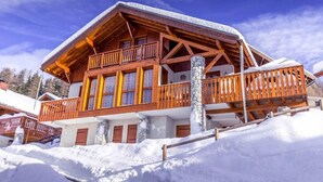 Una cabaña de madera con balcón y pilares de piedra, rodeada de nieve.