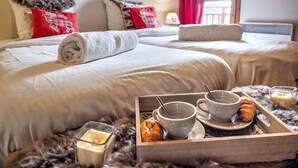 Habitación de hotel con dos camas, una bandeja de desayuno con cruasanes, tazas y una vela.
