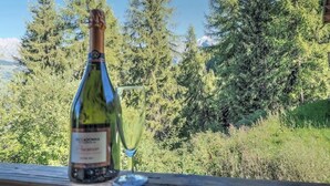 Eine Weinflasche und ein Glas auf einer Holztischplatte, im Hintergrund Wald und Berge.