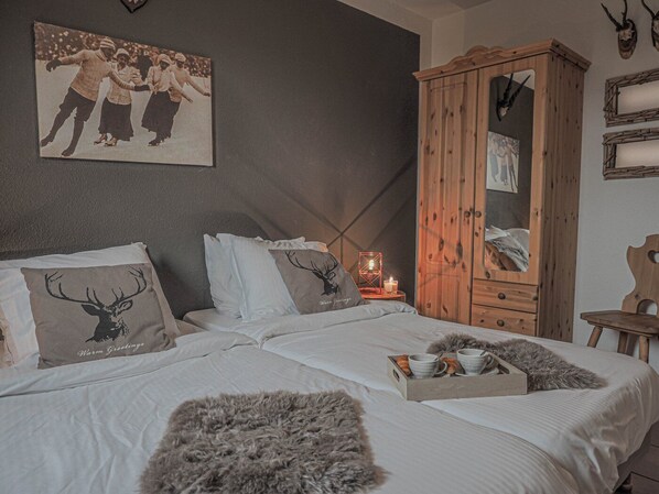 A bedroom with a bed, pillows, a wooden wardrobe, a mirror, and a wall-mounted picture.