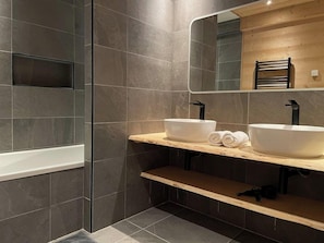 A modern bathroom with two sinks, a bathtub, and a wooden vanity.