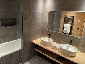 A modern bathroom with two sinks, a mirror, and a bathtub.
