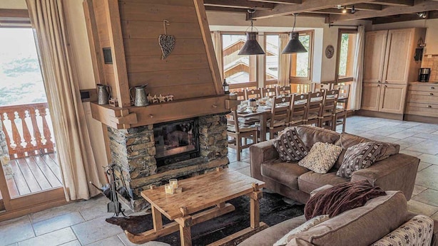 A cozy living room with a stone fireplace, wooden furniture, and a view of the outside. - Le Cairn, stunning 14 person, 7 bedroom chalet with sauna & games room (Peisey Nancroix)