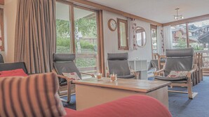 A cozy room with a sofa, two armchairs, a small table, and large windows offering a view of the outdoors. - Les Michailles 510 is a light, centrally located apartment for 8 (+2) people (Landry)