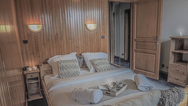 A bedroom with a wooden headboard, a bed with white linens, two wall-mounted lights, a wooden wardrobe, and a small bedside table with a lamp. - Les Michailles 510 is a light, centrally located apartment for 8 (+2) people (Landry)