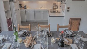 A modern kitchen with white cabinets, a dishwasher, and a dining area set for a meal with wine glasses, plates, and cutlery. - Les Michailles 510 is a light, centrally located apartment for 8 (+2) people (Landry)