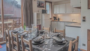 A dining area with a table set for six, a kitchen with white cabinets, and a view of a wooden building outside. - Les Michailles 510 is a light, centrally located apartment for 8 (+2) people (Landry)