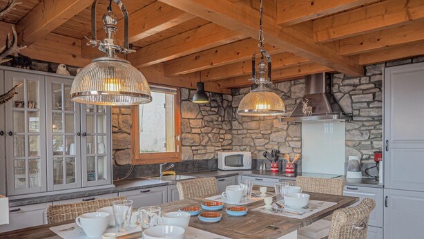 A rustic kitchen with a wooden island, stone walls, and hanging pendant lights.