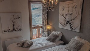 A bedroom with two beds, a chandelier, a window with curtains, and artwork on the walls.