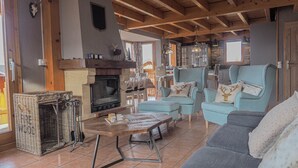 A cozy living room with a fireplace, comfortable seating, and a kitchen area in the background.