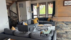 Un salon moderne avec un canapé d’angle, deux petites tables rondes et une cheminée en pierre.