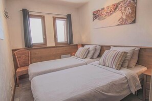 A bedroom with two beds, a chair, a window, and a wall painting.