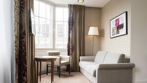Une pièce comprenant un canapé, une petite table, une lampe et une fenêtre avec des rideaux.