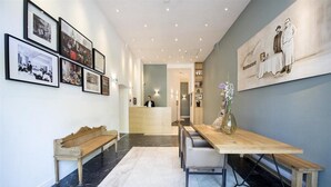 Un espace d’accueil comprenant un banc en bois, un comptoir de réception et un mur orné de photographies encadrées.
