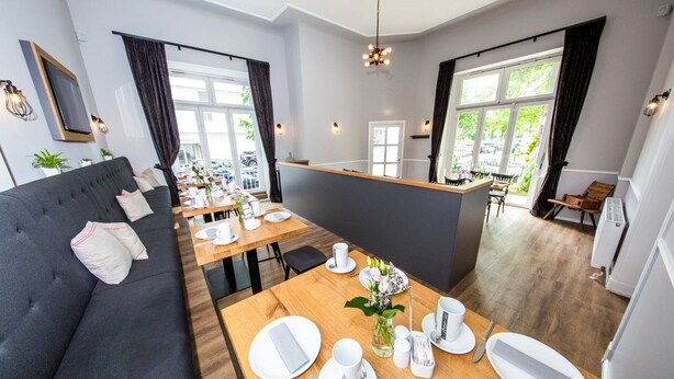 Ett modernt hotellrum med en soffa, ett matbord dukat med tallrikar, koppar och en vas med blommor.
