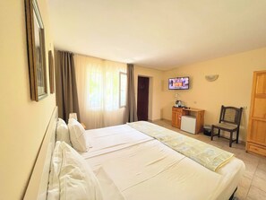 A hotel room with a large bed, a TV on the wall, a small desk, and a chair.