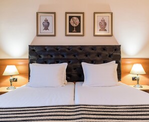 A double bed with a tufted headboard, two bedside tables with lamps, and three framed artworks on the wall. - Lotus (Nessebar)