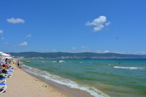 Una playa con cielos despejados, aguas tranquilas y montañas a lo lejos.