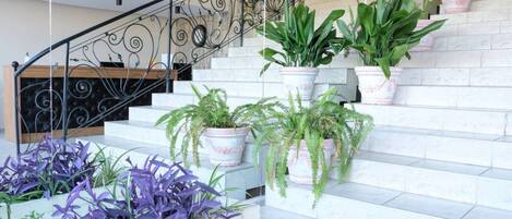 A staircase with white marble steps, surrounded by potted plants and a wrought iron railing.