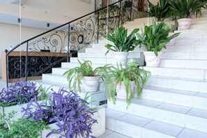 Una escalera con escalones de mármol blanco, rodeada de plantas en macetas y una barandilla de hierro forjado.