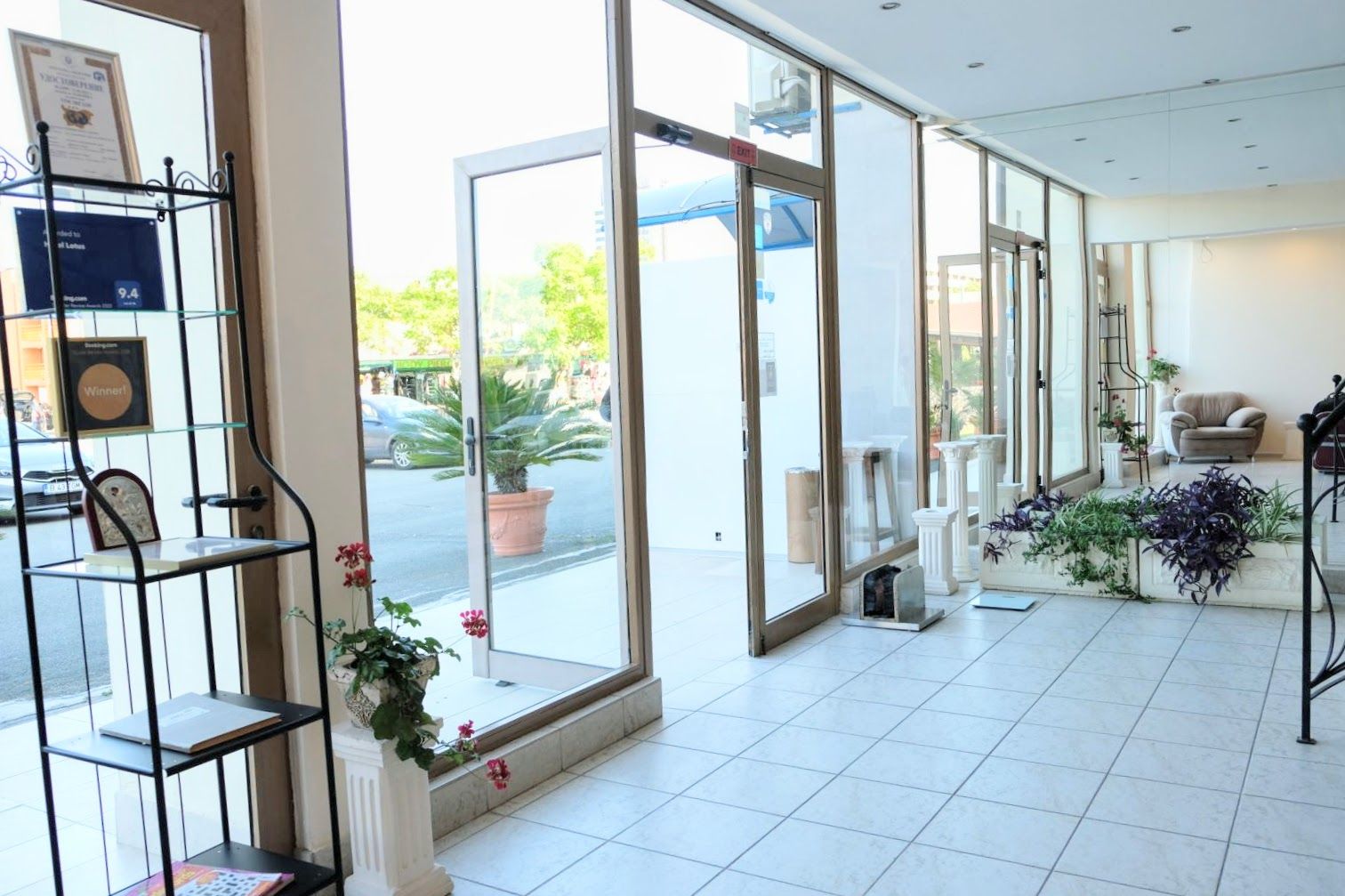 Vestíbulo de hotel con amplias puertas de vidrio, mostrador de recepción y plantas en macetas.