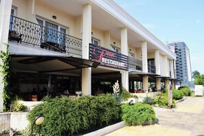 A restaurant with outdoor seating, a balcony, and a modern building facade.